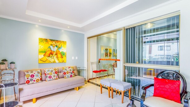 A modern living room with a grey sofa, colorful cushions, a large painting, and a view of the city through large windows. - Apt w/ Balcony Sudoeste - Por0017 (Sudoeste e Octogonal)