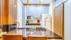 A compact kitchen with a gas stove, a microwave, and a refrigerator. - Apt w/ Balcony Sudoeste - Por0017 (Sudoeste e Octogonal)