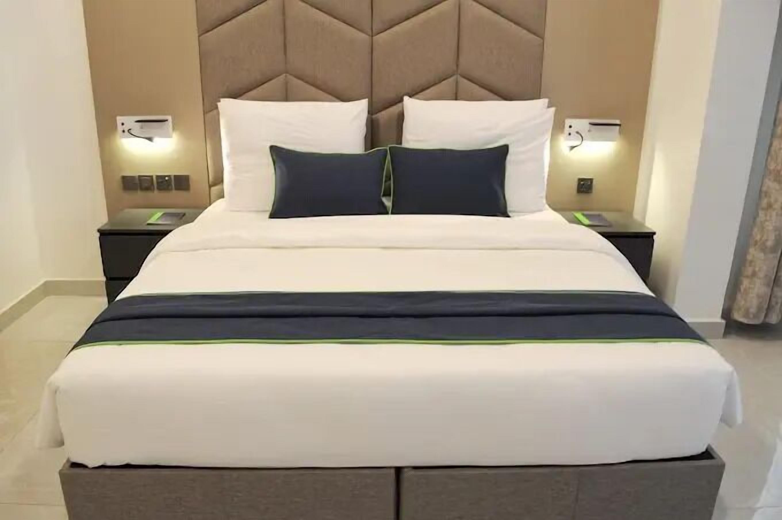 A neatly made bed with a headboard, two bedside tables with lamps, and a wall-mounted air conditioning unit.