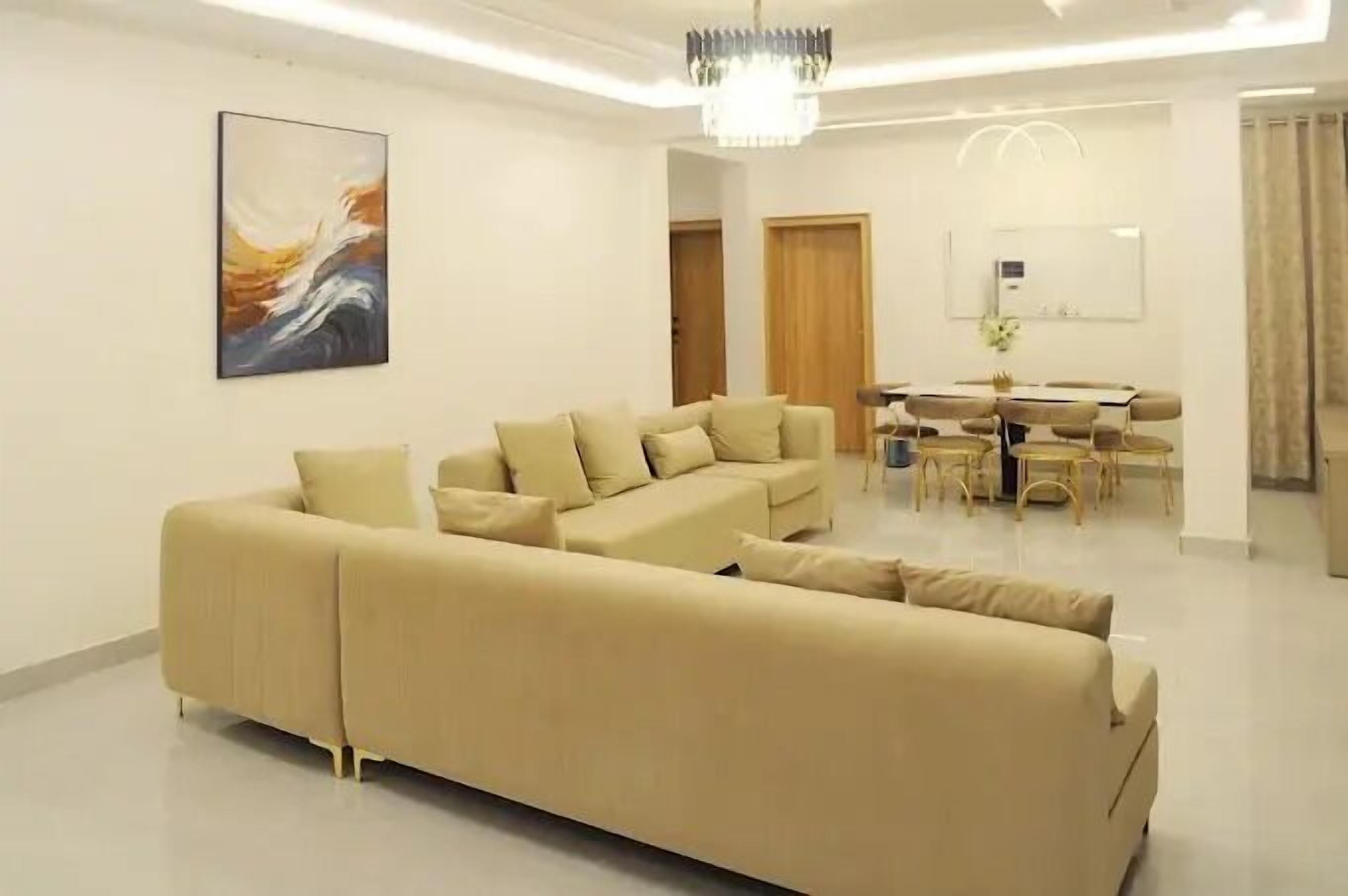 A modern living room with a beige sofa, a dining table with chairs, and a chandelier.