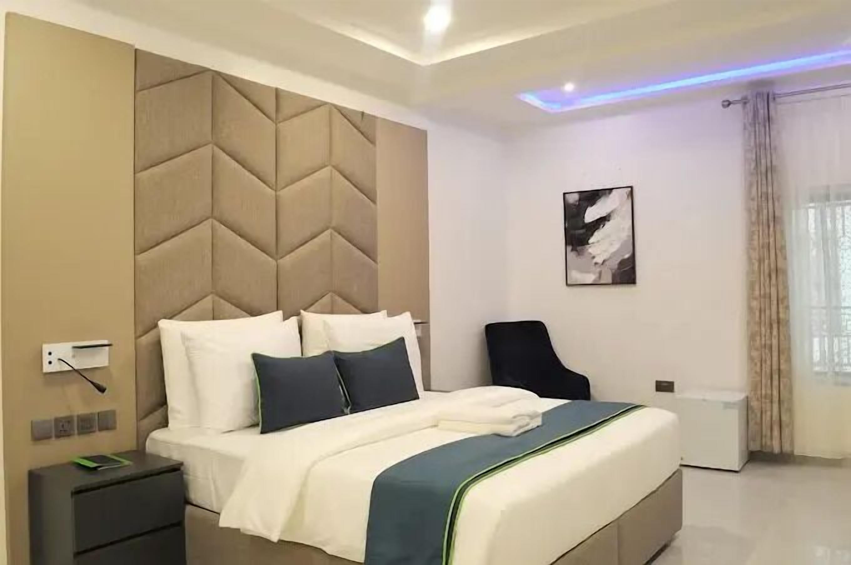 A modern bedroom with a large bed, a headboard, a bedside table, a chair, and a window with curtains.