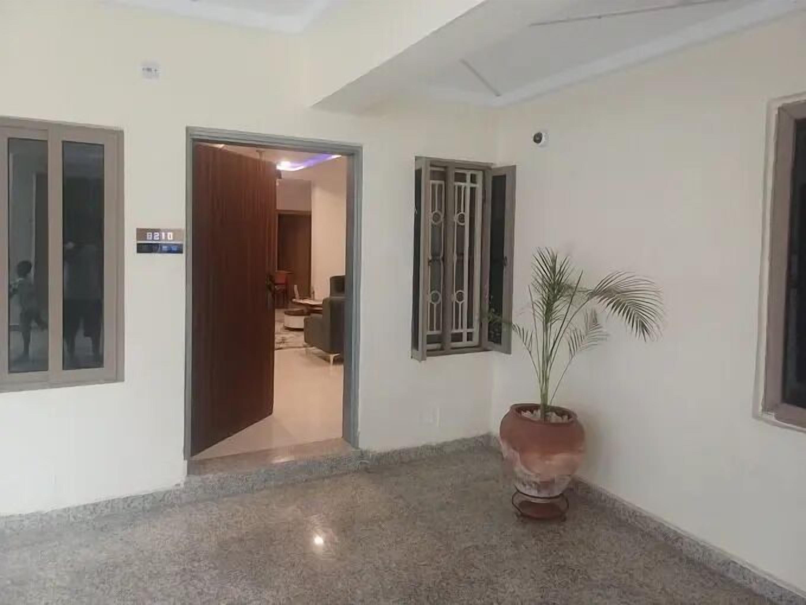 A hallway with a potted plant, a door with a number sign, and a window with bars.