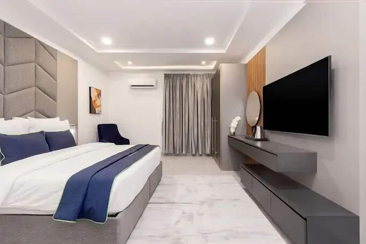 Un dormitorio de hotel moderno con una cama grande, un televisor de pantalla plana, una mesita de noche y un ventanal con cortinas.