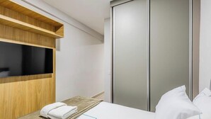 A hotel room with a wooden shelf, a flat-screen TV, a bed with white linens, and a sliding door closet. - Charming Studio Taguatinga Norte - Rjt0104 (Taguatinga)