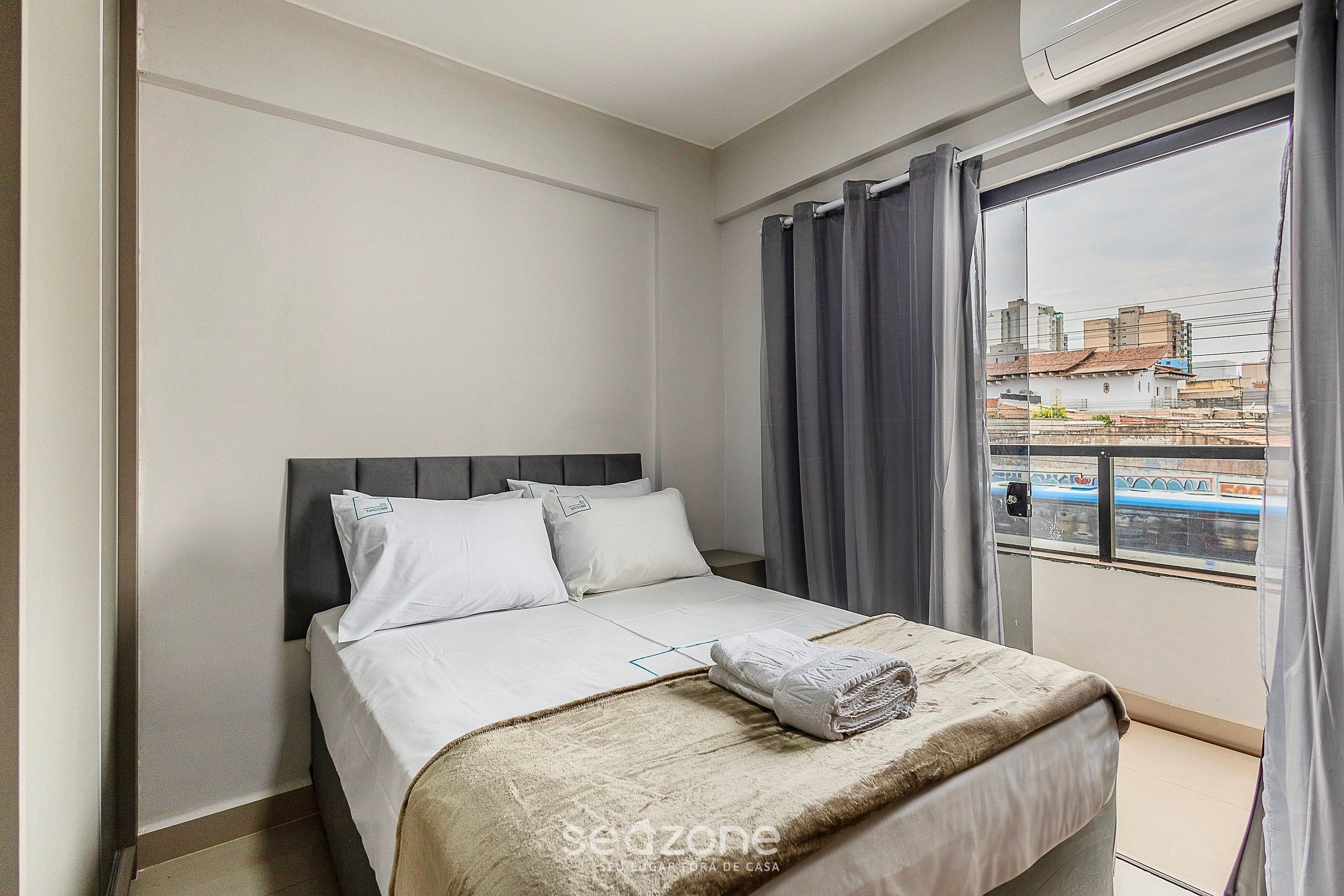 Ein Hotelzimmer mit Bett, Fenster mit Vorhängen und Blick auf Gebäude.