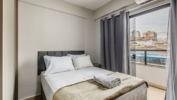 Ein Hotelzimmer mit Bett, Fenster mit Vorhängen und Blick auf Gebäude.
