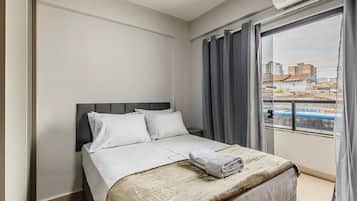 Ein Hotelzimmer mit Bett, Fenster mit Vorhängen und Blick auf Gebäude.