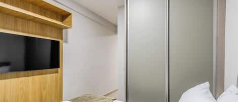 A hotel room with a bed, a television mounted on a wooden shelf, and a sliding wardrobe.
