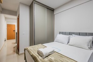 A hotel room with a bed, a wardrobe, and a door leading to another room. - Charming Studio Taguatinga Norte - Rjt0104 (Taguatinga)
