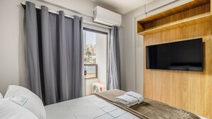Ein Hotelzimmer mit einem Bett, einem an einer Holzplatte montierten Fernseher und einem Fenster mit Vorhängen.