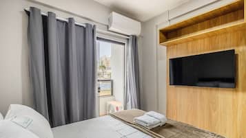 Ein Hotelzimmer mit einem Bett, einem an einer Holzplatte montierten Fernseher und einem Fenster mit Vorhängen.
