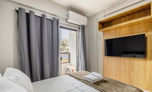 A hotel room with a bed, a TV mounted on a wooden panel, and a window with curtains. - Charming Studio Taguatinga Norte - Rjt0104 (Taguatinga)