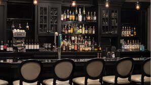Un espace bar avec de nombreuses bouteilles d’alcool, une machine à café et des tabourets de bar.