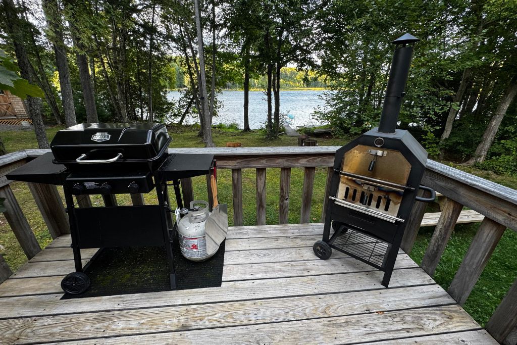 Une terrasse avec un barbecue et un fumoir, donnant sur un lac.