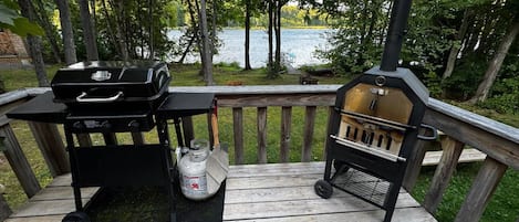 Um deck com churrasqueira e defumador, com vista para um lago.