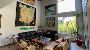 Un salon spacieux avec un plafond haut, une grande peinture, un canapé, une table basse et une plante en pot.