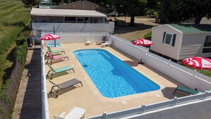 A rectangular swimming pool with lounge chairs and umbrellas, surrounded by a white fence and a wooden deck.