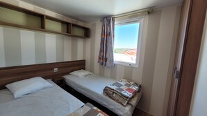 A small, single-room accommodation with two beds, a window with curtains, and a view of the outside.