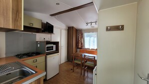 A compact kitchen with a gas stove, microwave, and a small refrigerator. There is a dining area with a table and chairs, and a window with curtains.