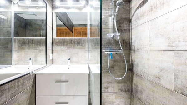 A modern bathroom with a glass shower enclosure, a white sink, and a wooden cabinet.