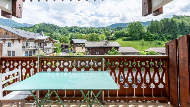 Un balcon avec une table et des chaises, donnant sur un paysage montagneux parsemé de bâtiments traditionnels.
