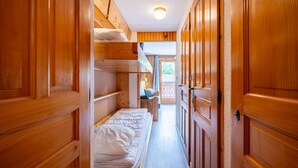 Un couloir étroit aux murs et aux portes en bois, qui mène à une pièce équipée de lits superposés et d’un petit coin salon.