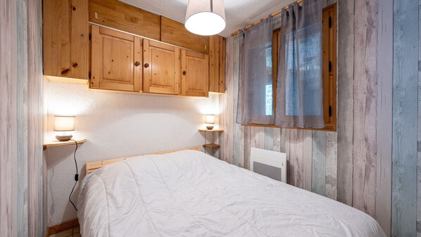 A bedroom with wooden walls, a bed, two bedside lamps, and a window with curtains.