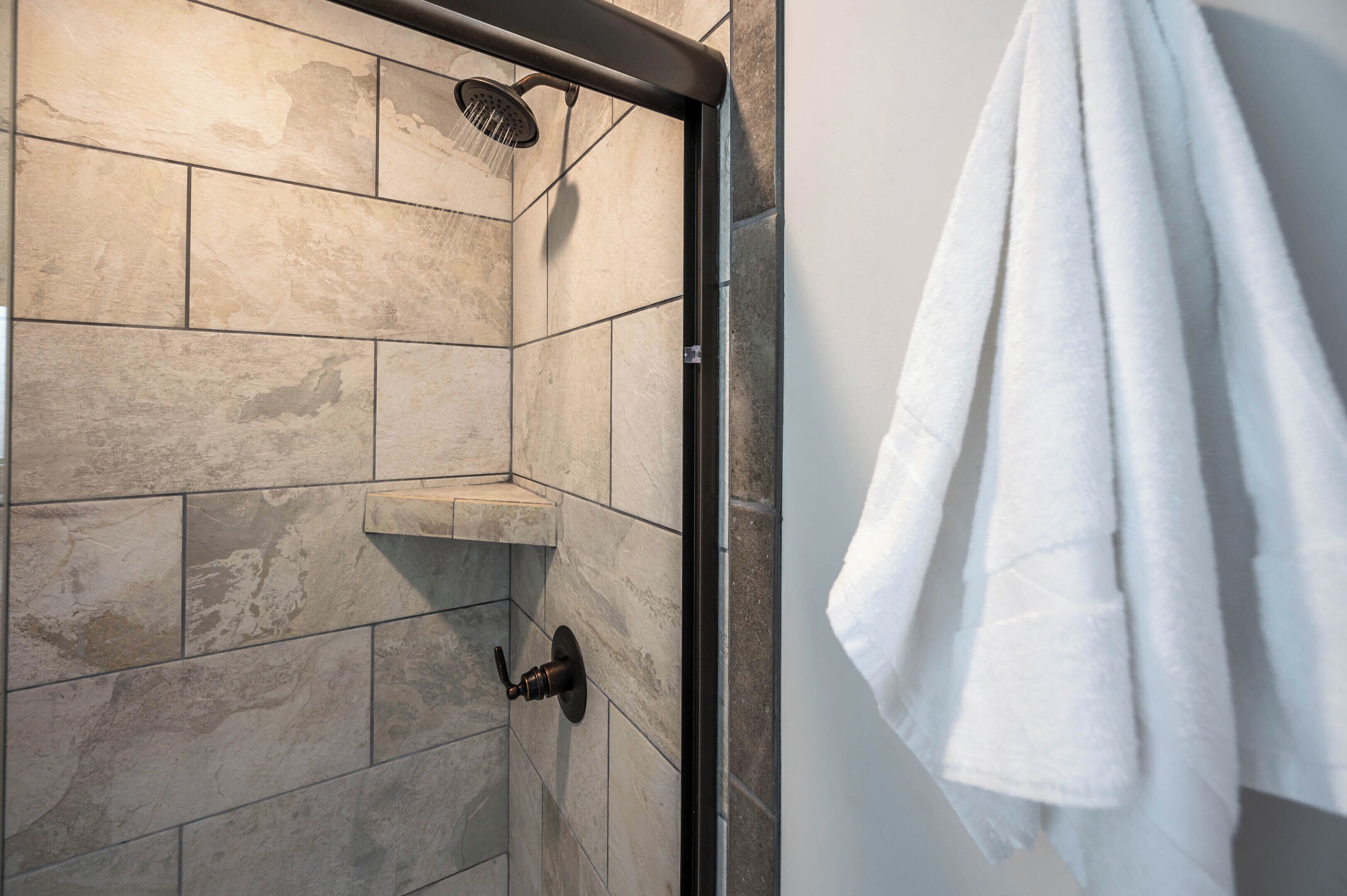 A shower area with a rain showerhead, a towel rack with a white towel, and a tiled wall.