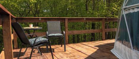 A wooden deck with two chairs and a table, surrounded by a wooden railing and a view of dense trees.