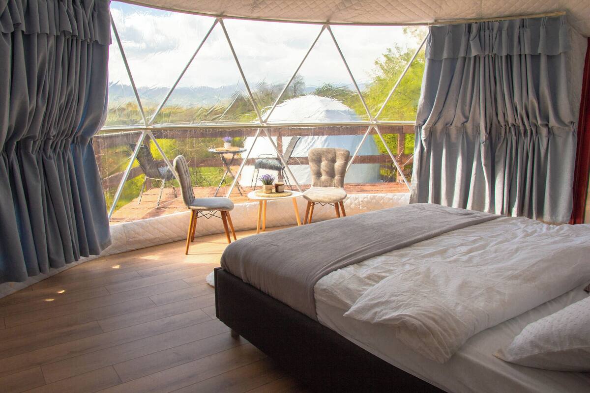 A bedroom with a large bed, two chairs, and a view of the outdoors through a window.