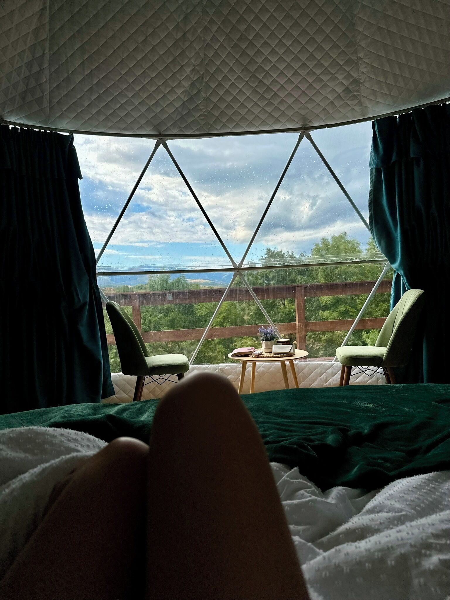 Ein Zeltraum mit Bett, zwei Stühlen, einem kleinen Tisch und Blick auf einen Weinberg.