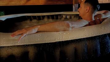 A person lying in a bathtub with a wooden headboard and a white towel.