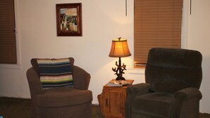 Een woonkamer met twee fauteuils, een houten bijzettafeltje met een lamp, en een schilderij in een lijst aan de muur.