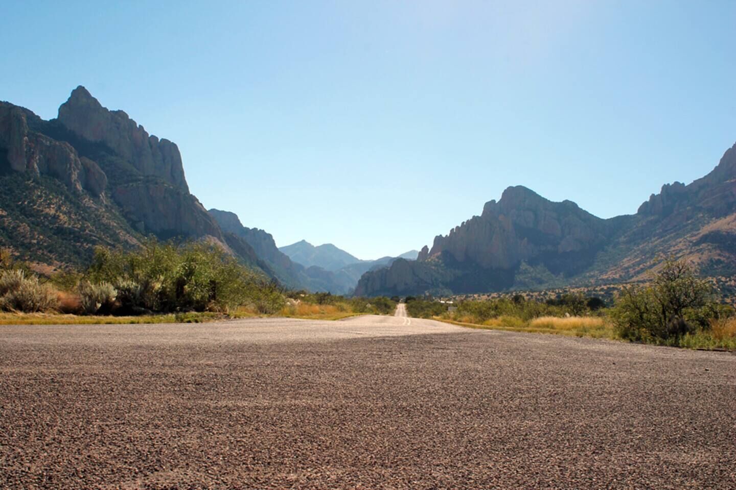 A paved road leading through a mountainous area with sparse vegetation.