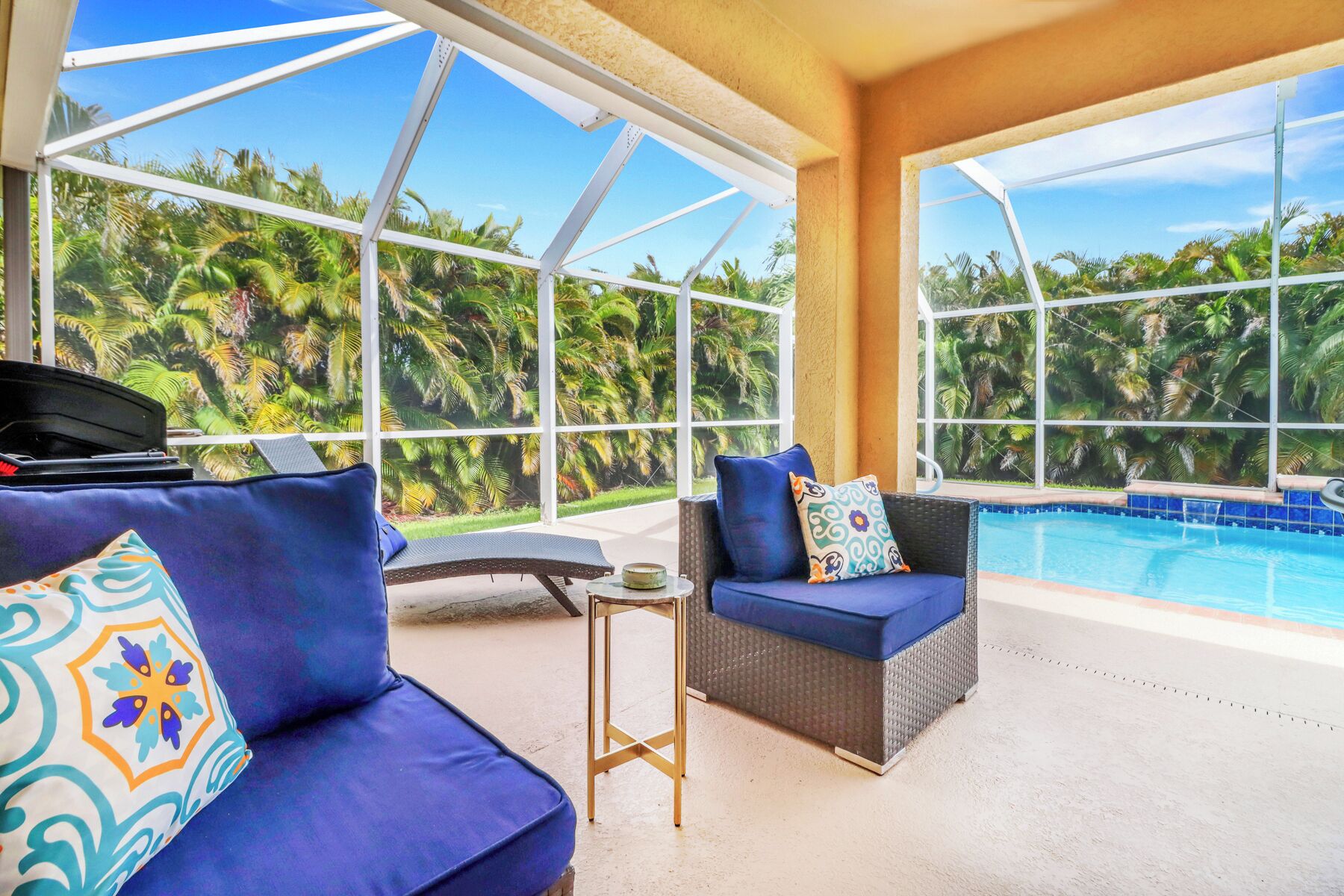 A sunlit room with a pool, large windows, and a sofa with a patterned pillow.