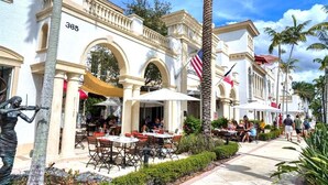 A building with a number '365' on the facade, outdoor seating with umbrellas, and palm trees.