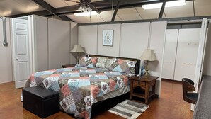 Un dormitorio con cama, mesitas de noche, ventilador de techo, una puerta y una pared con un cuadro enmarcado.