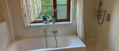 A bathroom with a large bathtub, a window with curtains, and a shower area.