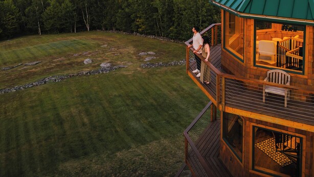 Eine Holzhütte mit einem grünen Dach, einem Balkon mit Sitzgelegenheit und Blick auf die umliegende Landschaft.