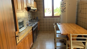 A kitchen with wooden cabinets, a stove, a sink, a refrigerator, and a window with a view of buildings outside. - Villa Panorama (Bivio Acquavella)