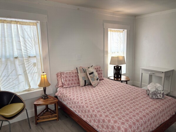 Un dormitorio con cama, mesita de noche, lámpara, silla y una pequeña mesa.