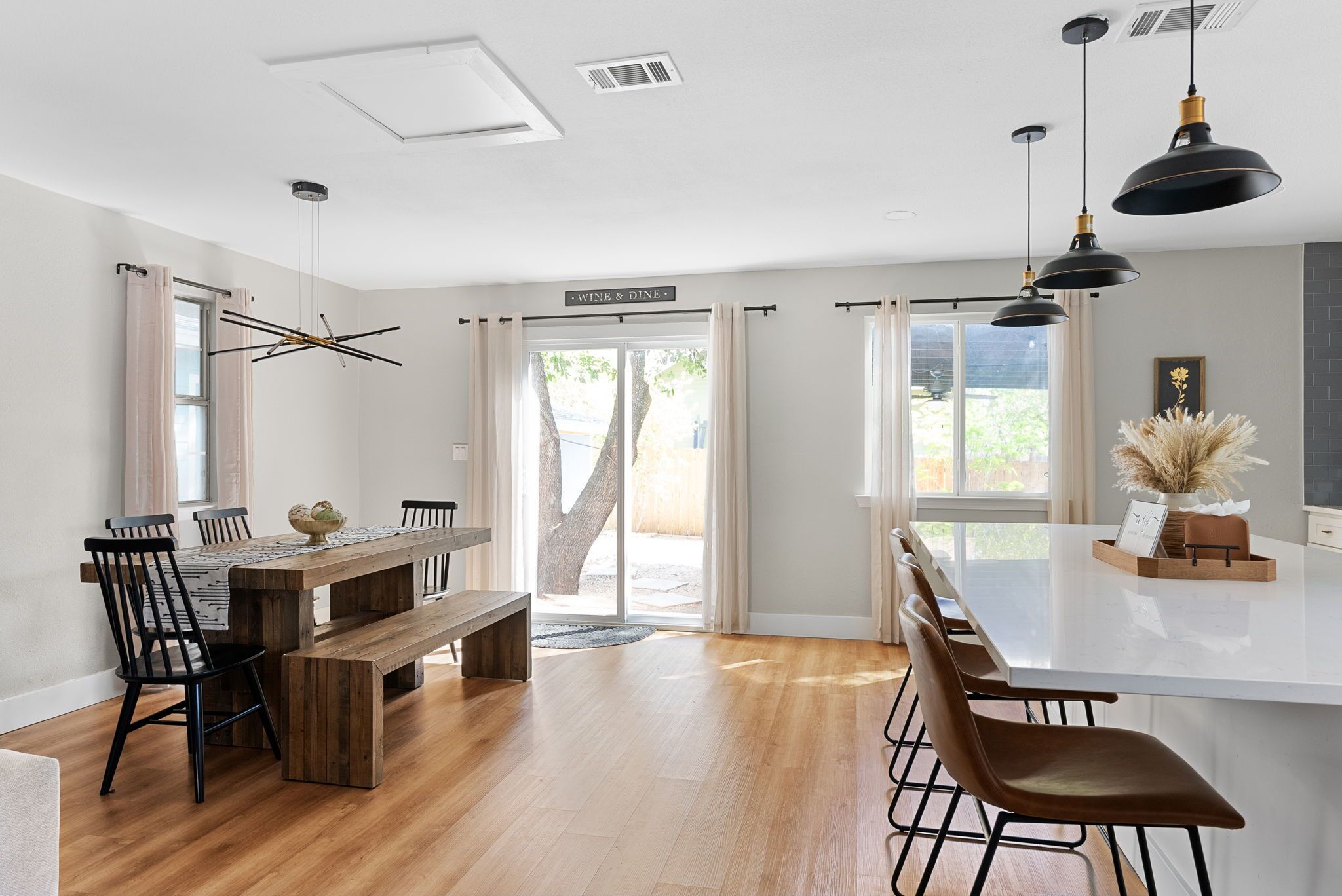 A modern kitchen with a wooden dining table, black chairs, and pendant lights.