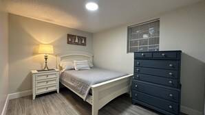 A bedroom with a bed, a dresser, a nightstand, a lamp, a window with blinds, and a ceiling light. - Charming 2-bedroom cottage in lovely Fort Walton Beach (Fort Walton Beach)