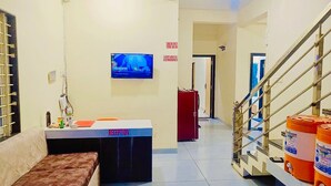 A reception area with a reception desk, a television mounted on the wall, and a staircase leading to another floor. - Hotel Rewanchal (Khandwa)