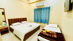 A hotel room with two beds, a TV, an air conditioner, and a bathroom with a mirror.