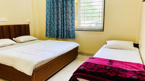 A bedroom with two beds, a window with blinds, and a curtain. - Hotel Rewanchal (Khandwa)