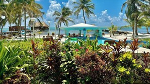 A resort with a pool, palm trees, and a beach view. - A3  Comfy 1BR Near Pool, Caribbean Sea Steps Away! (San Pedro)