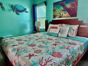 Un dormitorio con cama, mesita de noche, lámpara, decoración en la pared y ventana con cortinas.