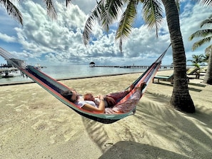 Una hamaca en una playa arenosa con cielo despejado y palmeras.
