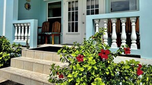 A building with a light blue exterior, a white door, and a set of stairs leading to a porch with a white balustrade. - A3  Comfy 1BR Near Pool, Caribbean Sea Steps Away! (San Pedro)